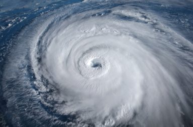 Aerial view of a large hurricane with a well-defined eye, swirling clouds, and vast spiraling bands over the sea.